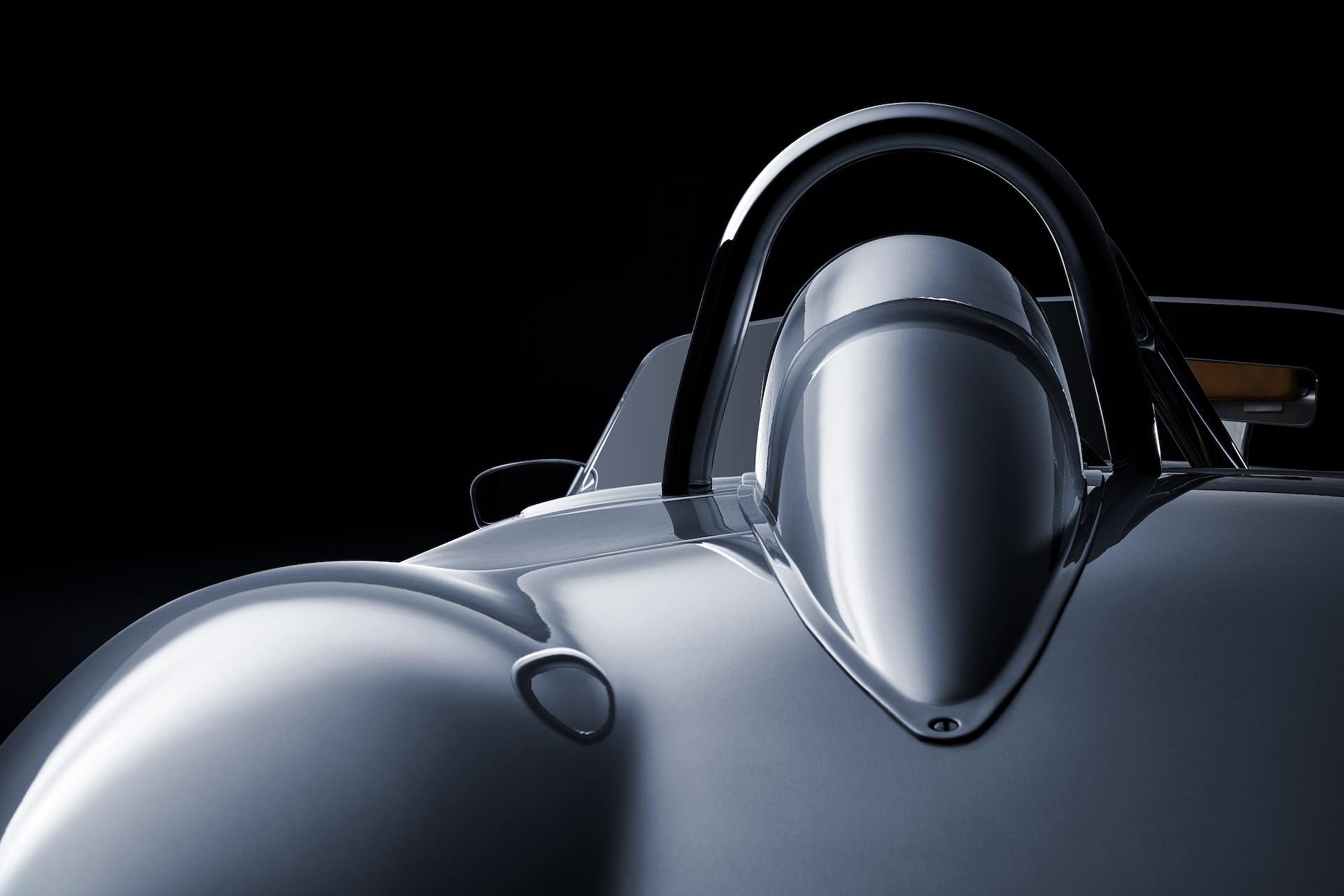 Nahaufnahme eines eleganten, silbernen Rennwagens mit offenem Cockpit vor schwarzem Hintergrund, der seine aerodynamischen Kurven und den Überrollbügel hervorhebt.