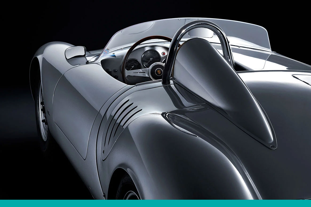 Rückansicht eines silbernen Porsche 550 mit offener Cockpit-Perspektive, edlem Lenkrad und markantem Überrollbügel.
