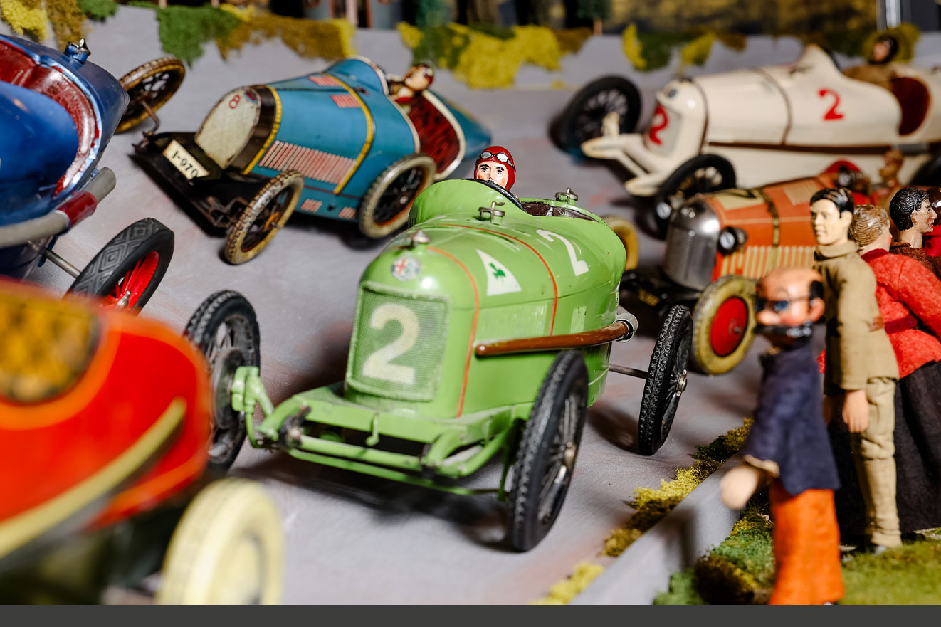 Detailreiche Szene mit historischen Blechspielzeug-Rennautos und Figuren auf einer Miniatur-Rennstrecke