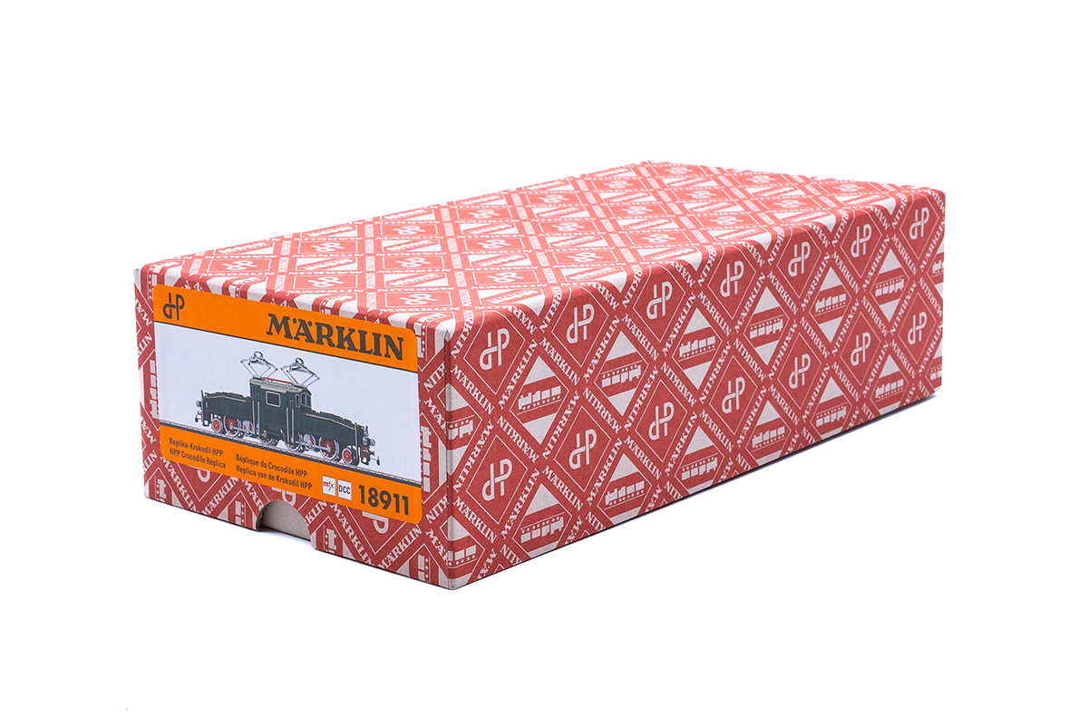 Eine rechteckige Märklin-Spielzeugeisenbahnschachtel mit einem rot-weiß gemusterten Design und einem orangefarbenen Etikett an einem Ende, das eine Zeichnung einer Zugmaschine und die Modellnummer 18911 zeigt.