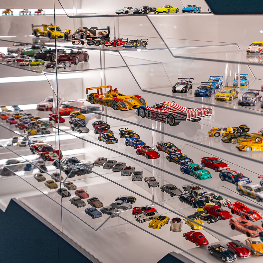 Eine Glasvitrine, gefüllt mit mehreren Regalen mit Spielzeugautos in verschiedenen Farben, Größen und Stilen, ordentlich angeordnet und von oben hell beleuchtet.